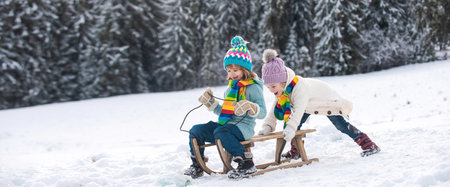 Funny children in snow ride on sled. Winter outdoors games. Happy Christmas family vacation concept. Kids enjoy the holiday.の写真素材
