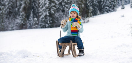 Boy sledding, enjoying sleigh ride. Winter vacation. Child sledding in winter snowy forest. Kids with sled, sleigh in winter snow, banner. Winter activities for kids.の写真素材
