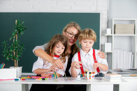 Back to school. School kids drawing with teacher. Children from elementary school study at pain...
