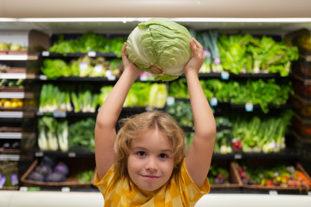 Child with cabbage. Kid in a food store or a supermarket. Little kid going shopping. Healthy food for kids.の写真素材