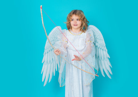 Angel child shoots a love arrow from a bow on Valentines Day. Child at angel costume. Kid with angel wings. Isolated studio shot.の写真素材