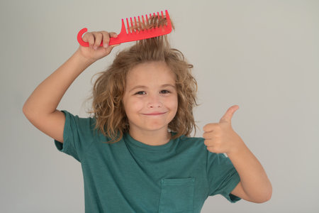 Boy brushes his hair. Cute child with comb. Blonde kid combs unruly hair. Kid boy with tangled long hair.の写真素材