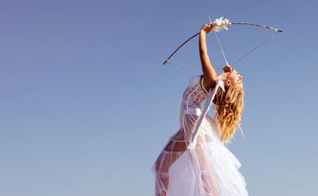 Banner. Angel teenager girl with white wings. Valentines day. Angel cupid with bow and arrow. Woman in white dress. Portrait of sweet angelic girl.の写真素材