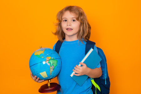Smart child, clever school kid. School boy hold world globe and book, isolated on yellow studio background. School and kids. Cute blonde child with a book learning. Knowledge day.の写真素材