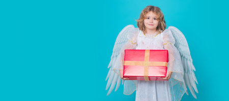 Cute child angel with gift box present. Child angel. Portrait of cute kid with angel wings isolated on studio background. Panoramic banner wide poster horizontal header.の写真素材