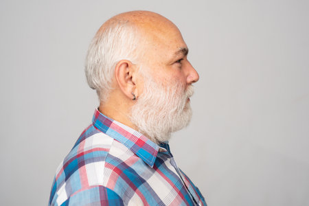 Mature man. Close up face of handsome elder senior in studio. Profile of old mature senior man with grey beard on gray isolated studio background.の写真素材