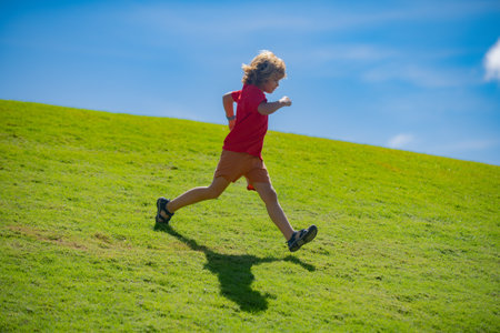 Sporty kid boy running on green grass and blue sky. Morning running with children. Child runner running in the nature. Morning jogging. Active healthy kids lifestyle.の写真素材