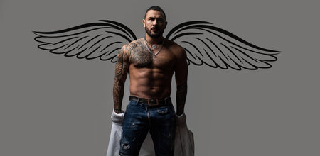 Photo banner of sexy man angel with wings for valentines day. Sexy man undressing shirt. Seductive face of a sexy man. Macho looking confident. Naked male shoulders, topless athletic body.の写真素材