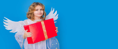 Kid boy angel with gift box present. Valentines day. Blonde cute child with angel wings on a blue isolated studio background. Banner header with copy space.の写真素材