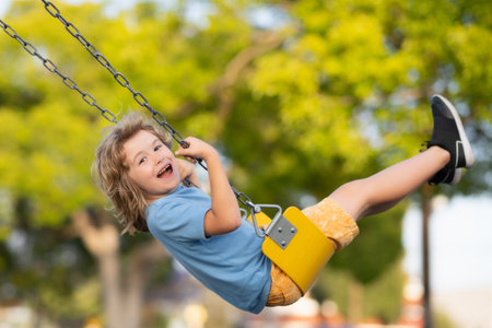 Outdoor playground. Funny kid on swing. Little boy swinging on playground. Happy cute excited child on swing. Cute child swinging on a swing. Crazy playful child swinging very high.の写真素材