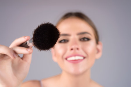 Close up makeup brush. Beautiful young woman applying makeup on studio background. Pretty girl holding makeup brushes and make up on face with cosmetics. Facial beauty. Perfect skin, natural make up.の写真素材