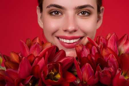 Happy smilig woman with flowers. Beauty girl with tulip. Beautiful sensual woman hold tulips bouquet, studio portrait on red background. Close up beauty woman face near tulips bouquet.の写真素材