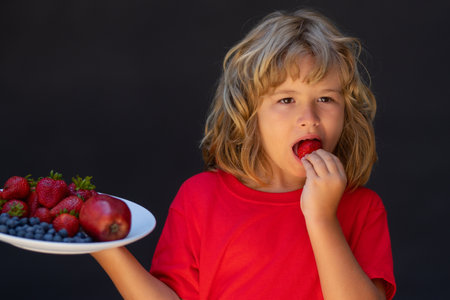 Kid hold plate of mix summer fruits. The child is picking strawberry. Kid eating ripe strawberry. Healthy organic strawberry fruit, summer season.の写真素材