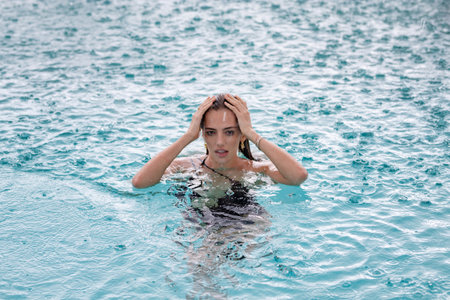 Rain in summer. Beautiful girl relaxing outdoor swimming pool. Enjoying summer vacation. Sexy woman...