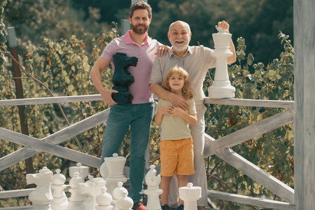 Excited grandfather father and son playing chess. Amazed men in different ages playing chess board...