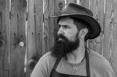 Portrait of farmer. Bearded gardener on wooden background. Handsome man spend time in the farm. Worker agriculture.の写真素材