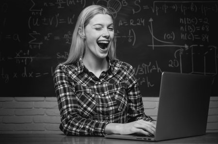 Female student looking at camera. Cheerful smiling girl student at the blackboard. College tutor. Student sitting at table and writing on notebookの写真素材
