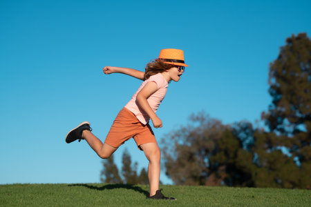 Kid boy running on green grass near blue sky in summer park. Healthy sport activity and running for children. Little boy at race. Young athlete in training. Runner exercising. Jogging for kid.の写真素材