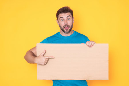 Man holds sign, blank card. Placard ready for your product. Sign to your text. Man showing blank sign board over studio isolated background, pointing finger. Empty blank board. Area for advertising.の写真素材