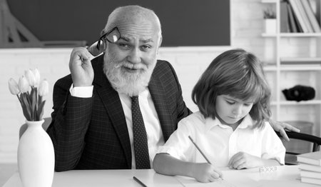 Help to learn. Old teacher with pupil. School lesson. Education concept. Old teacher with schoolboy in classroom.の写真素材