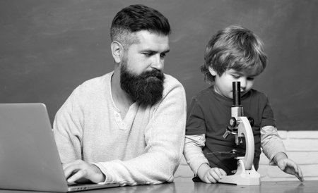 Teacher helping pupils studying on desks in classroom. Young boy doing his school homework with his father. Chalkboard background. Dad son are concentrated on the problem.の写真素材