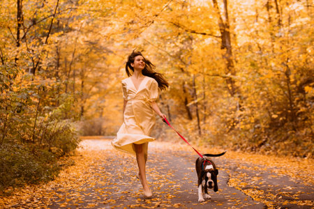 Young woman with the dog in the park. Wind in the hair. With dog on a walk in an autumn nature. Young beautiful female having fun in autumn park. Girl enjoy walk with dog. Favorite pet.の写真素材