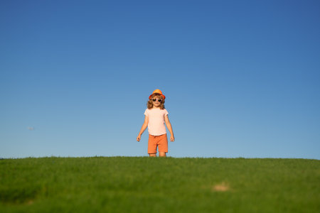 Kid boy running on green grass near blue sky in spring park. Sporty child boy runner running in summer park. Active kids, sport children.の写真素材
