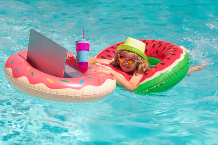 Summer travelling. Kid working on laptop computer at poolside swimming pool. Summer online technology. Traveler relaxing on tropical sea in summer holidays. Freelance work concept.の写真素材