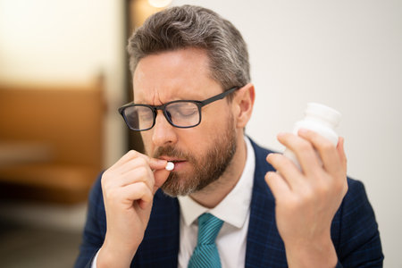 Millennial Businessman in office having headache. Man taking a medicine pill from headache migraine.の写真素材