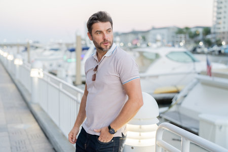 Portrait of handsome male model outdoor. Stylish man dressed in polo. Fashion male posing on the street background. Urban style. Rich man dreaming about riches near the yacht.の写真素材
