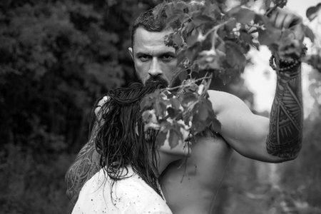 Sensual cople in love. Brutal bearded man holding rose ramification and embracing his beautiful woman. Eternal love and trust concept.の写真素材