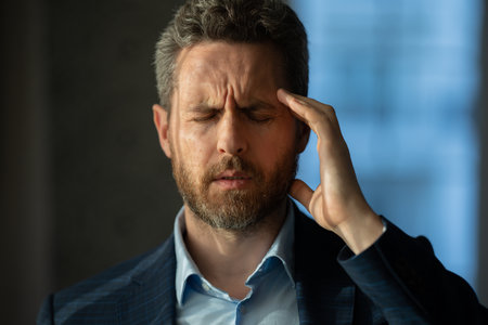 Tired man having a terrible headache. Exhausted man feeling unhealthy, upset about headache illness. Closeup portrait of stressed middle-aged man having headache. Migraine and headache concept.の写真素材