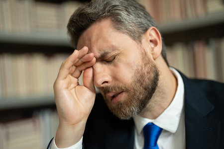 Close up portrait of stressed man with headache migraine. Tired businessman is working overtime and has headache. Man with laptop at workplace, suffers from headache. Migraine from overwork.の写真素材