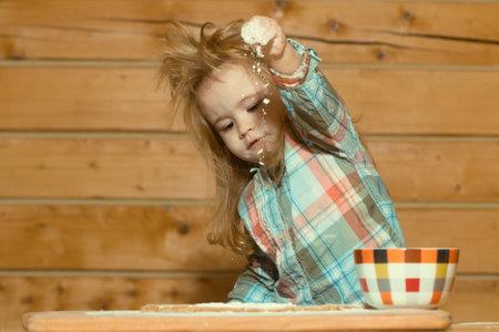 Fun image of baby chef play with flour on wooden kitchen background. Baby kid doing homemade bakery in kitchen. Child sitting on table and enjoy learn to cooking foods or baking.の写真素材