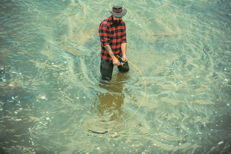 Bearded man fly fishing. Cheerful fisherman fishing in a river outdoors. Fishing as holiday. Stand in water. Man fishing on the river. Good profit.の写真素材