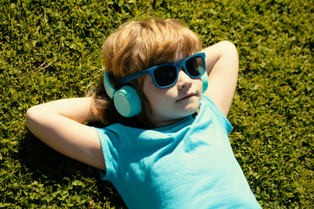 Listening to music. Summer boy in headphones. Kid in park lying on grass.の写真素材