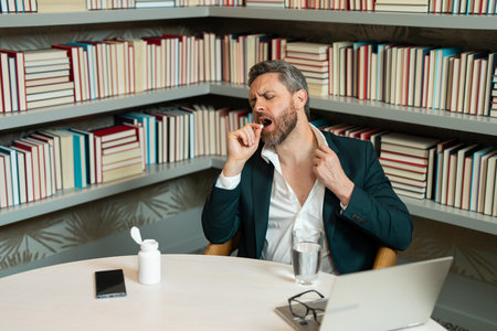 Man taking a medicine pill from headache migraine. Overworked man feeling migraine head strain. Tired bored man has office syndrome. Exhausted man work on laptop struggle with migraine.の写真素材