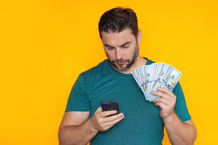 Man holding cash money in dollar banknotes on isolated yellow background. Studio portrait of...