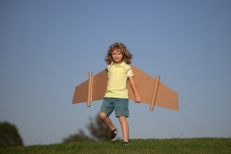 Child boy plays pilot astronaut. Kid dreaming of becoming a aviator spaceman. Child playing with a cardboard wings plane in summer green grass field outdoor.の写真素材
