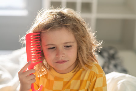 Boy brushes his hair. Child with tangled blonde long hair tries to comb it. Hair portrait kid with a comb.の写真素材