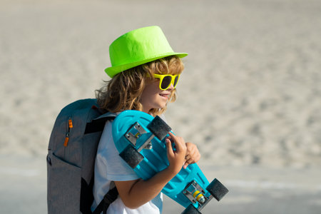 Childhood. Cute child with skateboard on street background. Funny kid boy, stylish skater holding skateboard outdoor.の写真素材