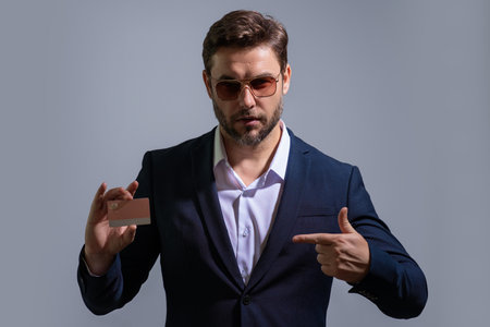 Business man holding credit card over isolated studio gray background. Businessman with credit bank card, recommend bank discounts. Credit card for e-banking, e-commerce, cashback transaction.の写真素材