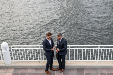 Cheerful middle eastern businessman walking by street towards modern office building. Portrait of successful business people outdoor, talking together in urban background.の写真素材