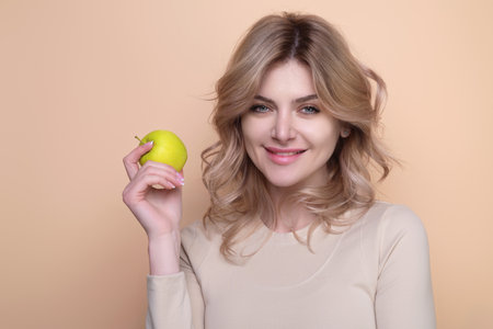 Tasty and juicy apple. Young sexy woman eating apple, studio portrait. Morning breakfast with vitamin. Woman holding apples with healthy teeth. Woman biting apple isolated over beige background.の写真素材