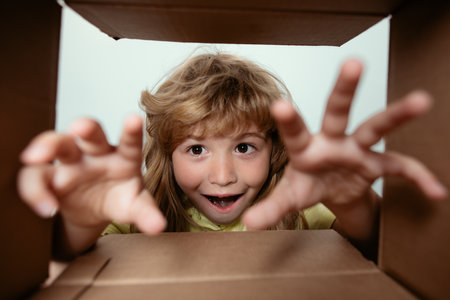 Funny excited child unpacking and opening the carton box looking inside. The little kids unboxing gift inside view. Child boy looking surprised into a gift.の写真素材