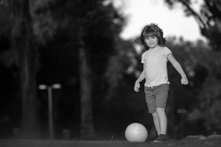 Little kid boy playing football in the field with soccer ball. Concept of children sport. Child playing football on the playground in park.の写真素材