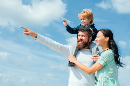 Daddy, mommy and child son. Happy family - child son playing with paper airplane. Portrait of happy father giving son piggyback ride on his shoulders, hug wife and looking up.の写真素材