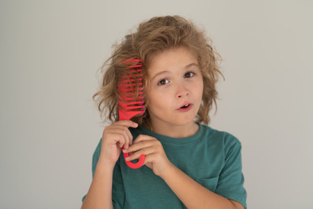 Comb and hair brush concept. Cute funny child with curly blonde hair holding comb hairbrush for combing. Little kid combing hair, isolated studio background.の写真素材