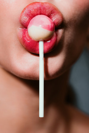 Closeup of sucking a lollipop. Sexy woman with red lips holding lollipop, beauty close up. Sexual lips with candy, sexy sweet dreams. Attractive female mouth licks chupa chups, sucks lollipop.の写真素材