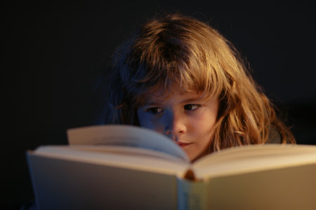 Child reading a magic book in bed. Kid boy read books at home. Bedtime stories fairy story before bed.の写真素材